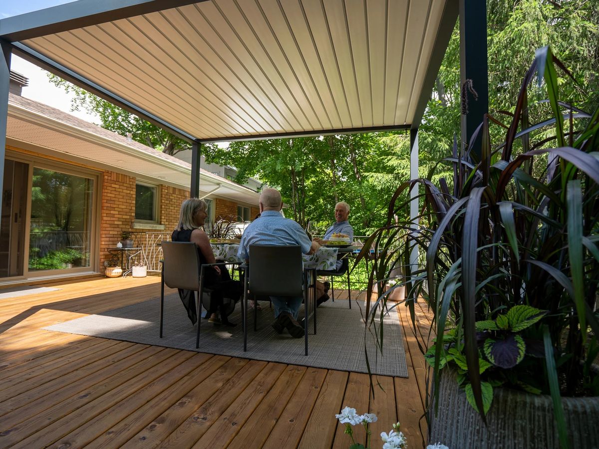 Family under a louvered pergola with the louvers closed during a light rain in Round Rock