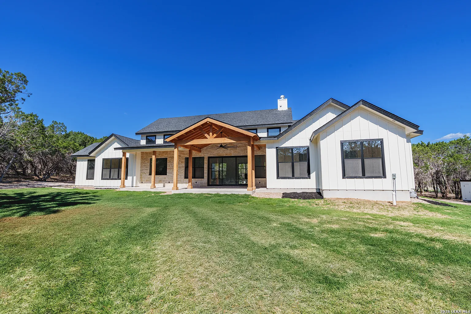 Cedar patio cover with exposed rafters and a matching shingle roof on a limestone home in Round Rock