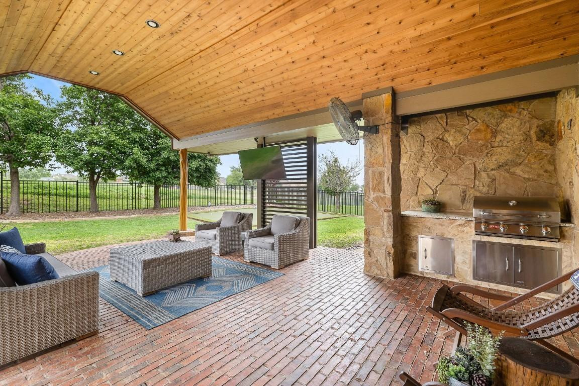 Stone outdoor kitchen island with grill and bar seating under a covered patio in Round Rock